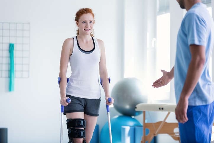 Woman walking with brace and crutches during physiotherapy Woman walking with brace and crutches during physiotherapy